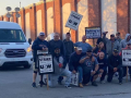 A group of striking steelworkers pose for a photo in a driveway, while a van carrying replacement workers waits behind them.