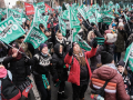 People cheer in a massive packed outdoor crowd with light green flags that say “We are of one voice” in French