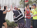 A woman in a safety vest high-fives two others in front of a fence while others stand by with strike signs