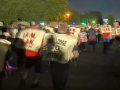 A crowd of workers walk away from the camera at night wearing tabards reading “District Lodge 70 on strike”