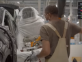 A masked worker in overalls place a seat into a car on an assembly line.