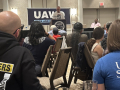 An audience listens to a man at a lectern. One audience member has a blue shirt with “Union Strong” on the back.