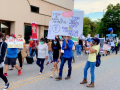 Masked people march with signs: "Tyson Is Killing Us for Profits. Tyson Treats the Workers Worst than the Chickens We Process." "Don't Believe Tyson." "Shut Down the Factories." "Protect = Respect." 