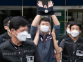 Man in mask raises handcuffed hands in air, escorted by several other masked men whose jackets read "POLICE"