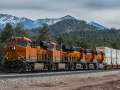 An orange BNSF train passes in front of a mountain and forested hills