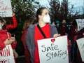 Three women dressed in red hold hand-lettered signs: "Safe Staffing Saves Lives" and "Patients Over Profits"