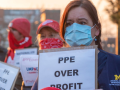 Masked workers in University of Michigan RN stand outside at dusk or dawn carrying home-printed signs: "PPE OVER PROFIT"