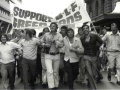 Black and white photo of men marching with a banner: "SUPPORT BLF GREEN BANS"