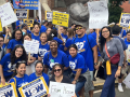 A group of 25 fired-up nurses in royal blue t-shirts poses with signs about striking and safe staffing.