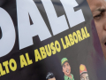 Un hombre grita mientras sostiene un cartel que dice DALE Alto Al Abuso Laboral