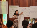 Woman leads organizing meeting from front of room.