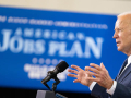 sideview of President Joe Biden speaking at a podium at Pittsburgh Carpenters Hall on March 31, 2021, with American Jobs Plan sign in background (white on blue)