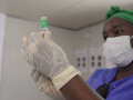 Medical officer in blue scrubs, green bandana, and surgical mask preparing vaccine for administration