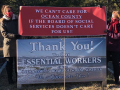 Two workers hold a banner reading “We Can't Care for Ocean County If the Board of Social Services Doesn’t Care About Us!” over the “Thank You to Our Essential Workers” sign that the Board had put up.