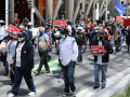 Masked people marching outside. Some have signs: "UNLOCK THE MONEY," "FREE OUR FUNDING," "AUSTERITY IS RACIST!"