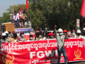 Dozens of workers march behind a red banner in Myanmar. Some carry red flags.