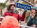 A woman speaks at a strike rally while another woman interprets in sign language. Behind them is a palm tree, an apartment buidling or hotel, and a street sign "Boylston"