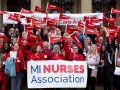 Large crowd of Michigan Nurses Association members posing in red with flags and banner on steps assembled.