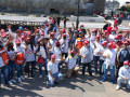 A group of fifty workers red hats and white shirts raise their fists and pose for the camera