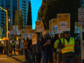 Picketers in yellow vests holding "ON STRIKE FOR FAIR WAGES AGAINST SELLER CONSTRUCTION" signs outside in dim dawn light.