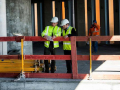 Two construction workers looking down in building construction site with wooden scaffolding around them.