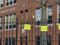 handwritten signs "we miss you" hang on the fence outside a brick building labeled Hartford University School